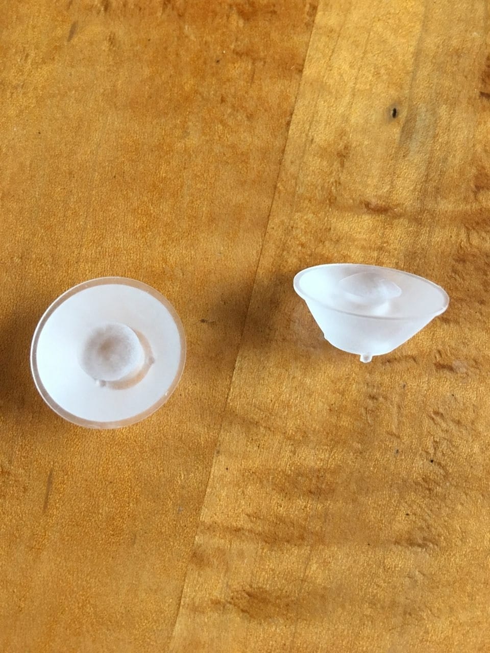 Machined and hand-polished PMMA prototype lenses — round symmetric early version and asymmetric teardrop final design